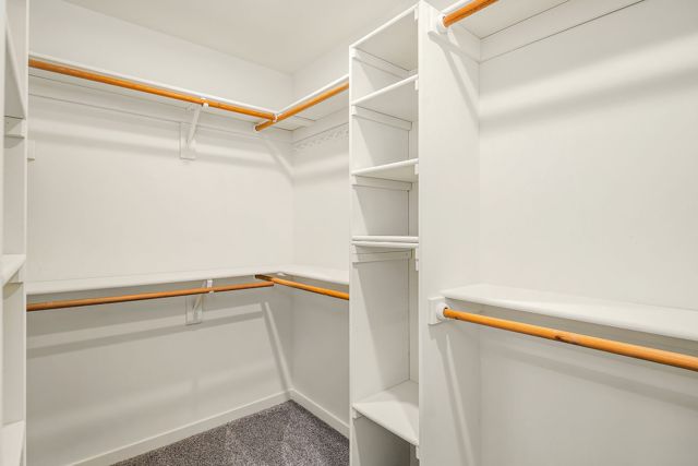 Empty walk-in closet with white melamine shelving and wood rods